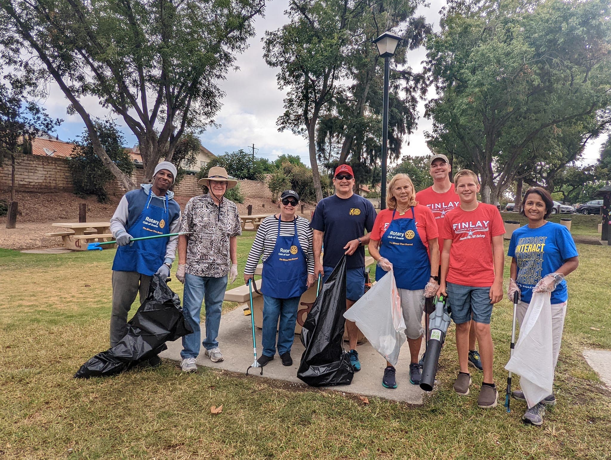 Diverse volunteers posing in a park with trash bags and tools for community cleanup.
